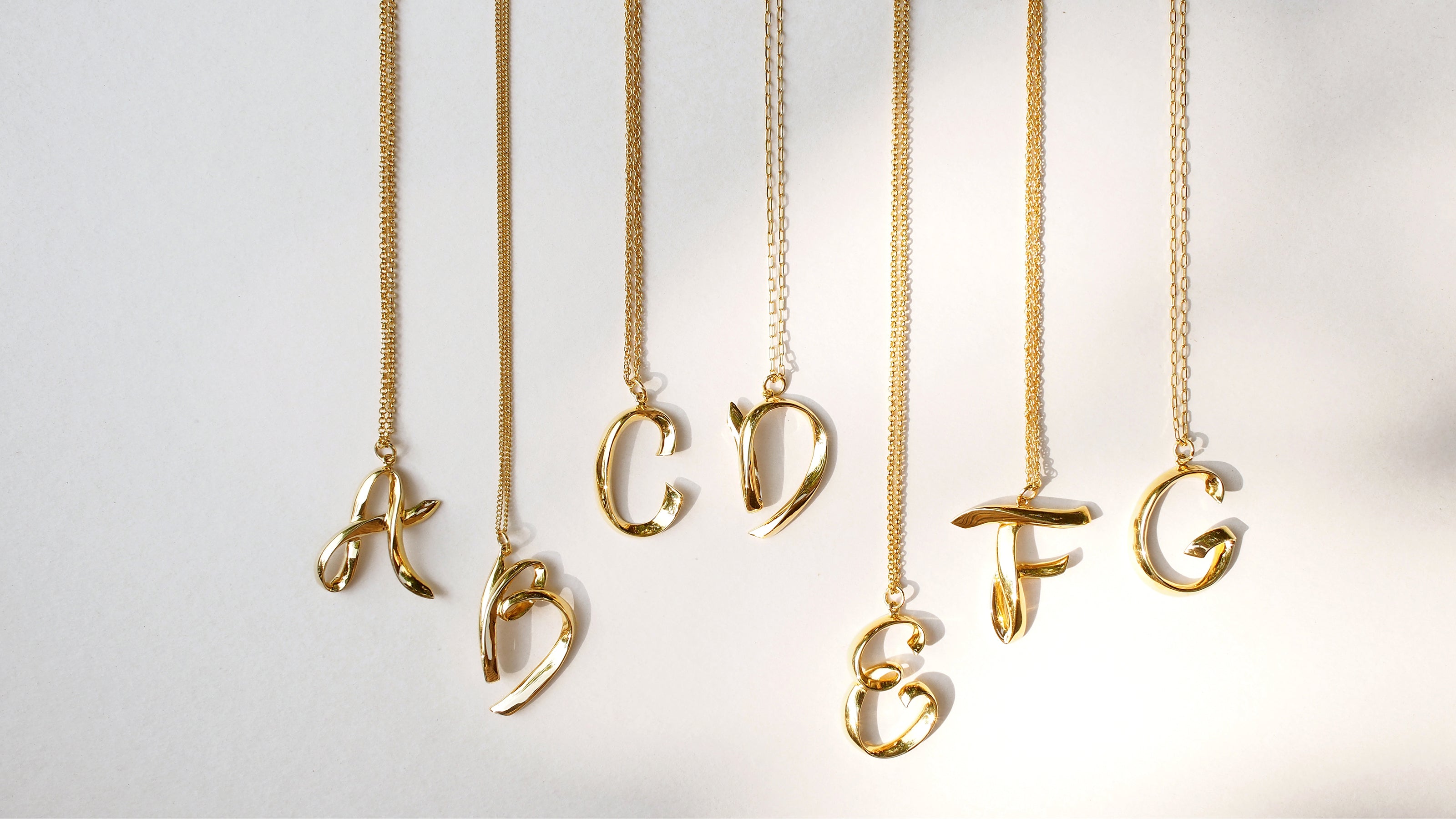 Elegant gold color necklaces with artistic initials A, B, C, D, E, F, and G displayed on various chain styles.