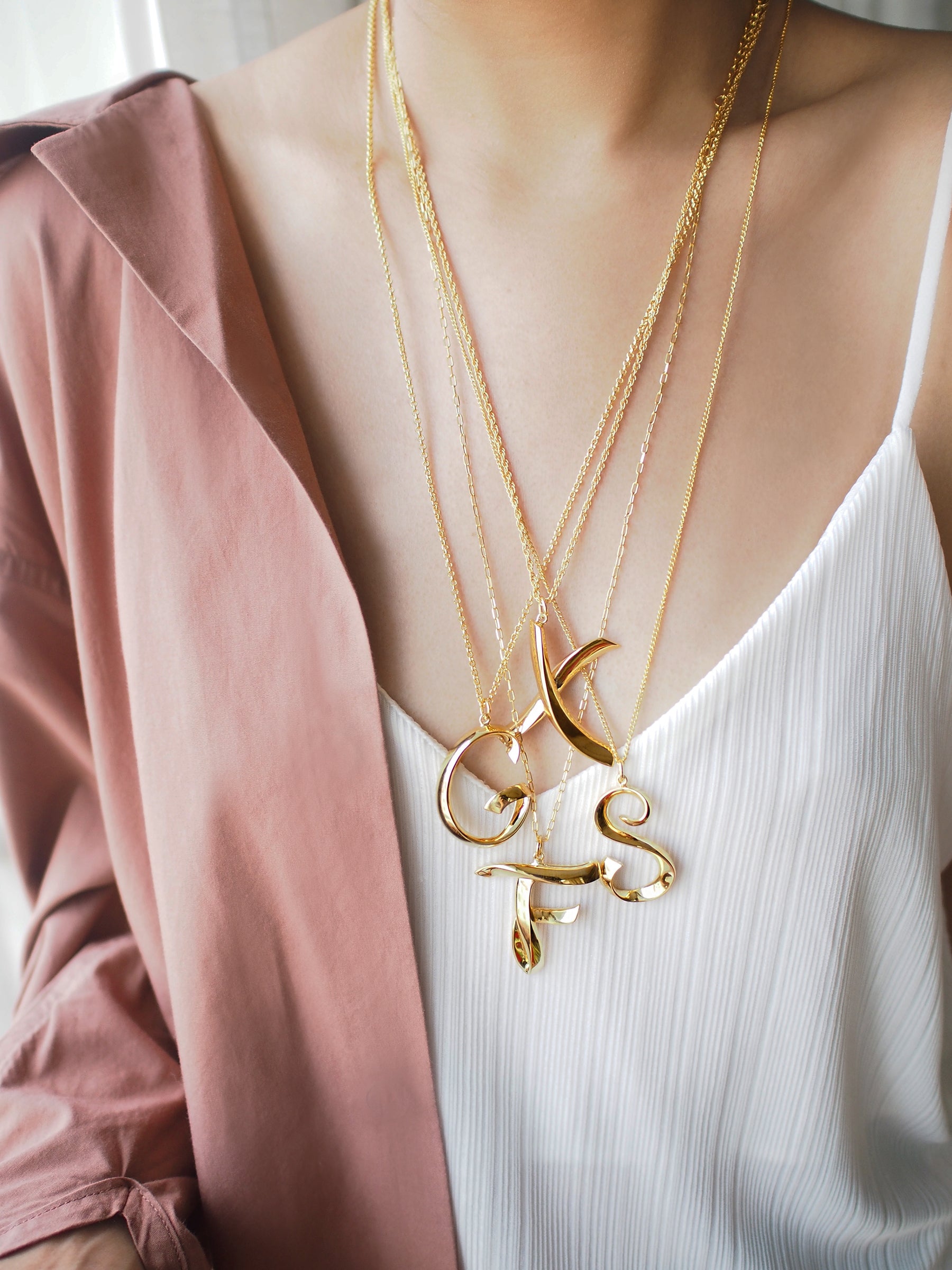 Close-up of fashionable layered letter necklaces on a model.