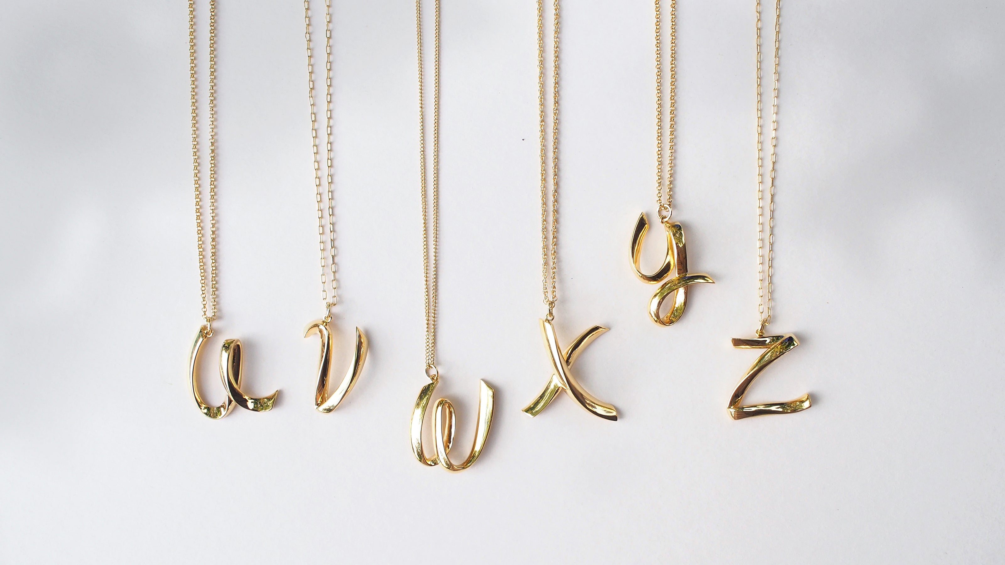 Personalized gold-colored necklaces with initials U, V, W, X, Y and Z displayed on various chain styles.