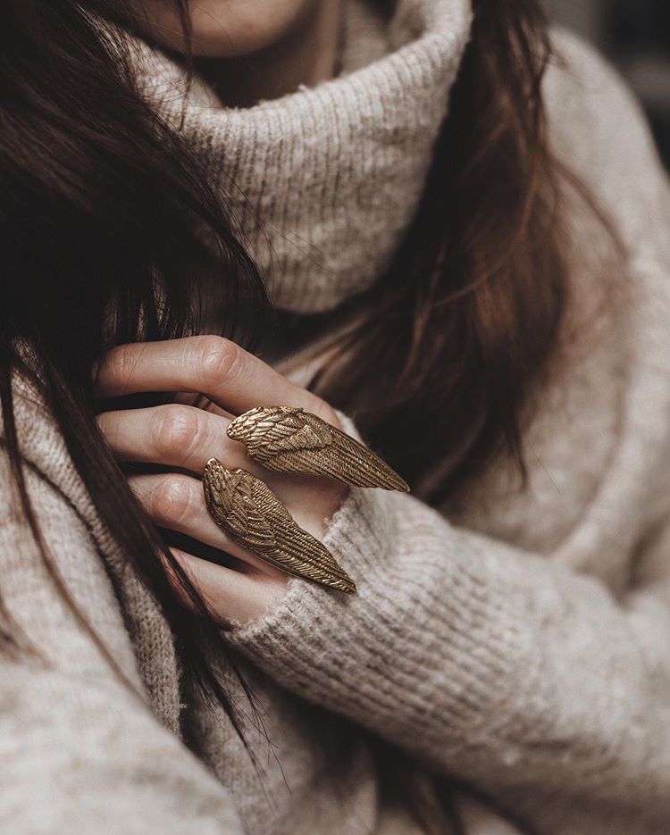 A beautiful golden wing ring worn on a hand,  paired with a cozy sweater.