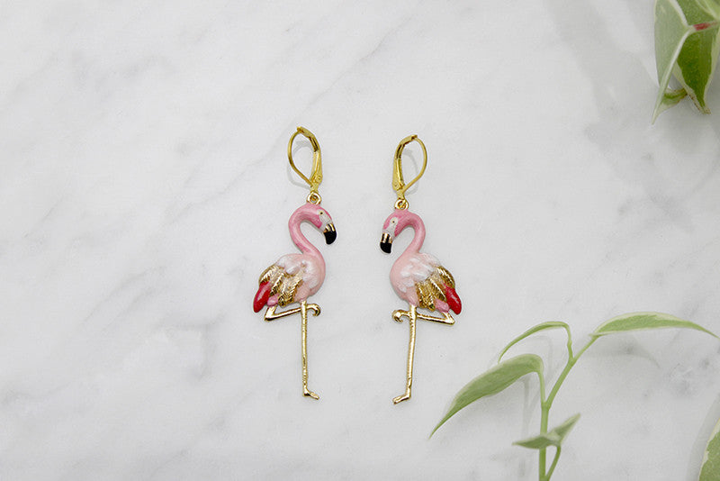 Eye-catching earrings designed in the shape of flamingos placed on marble background.