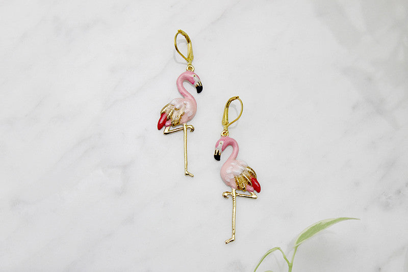 Eye-catching earrings designed in the shape of flamingos placed on marble background.