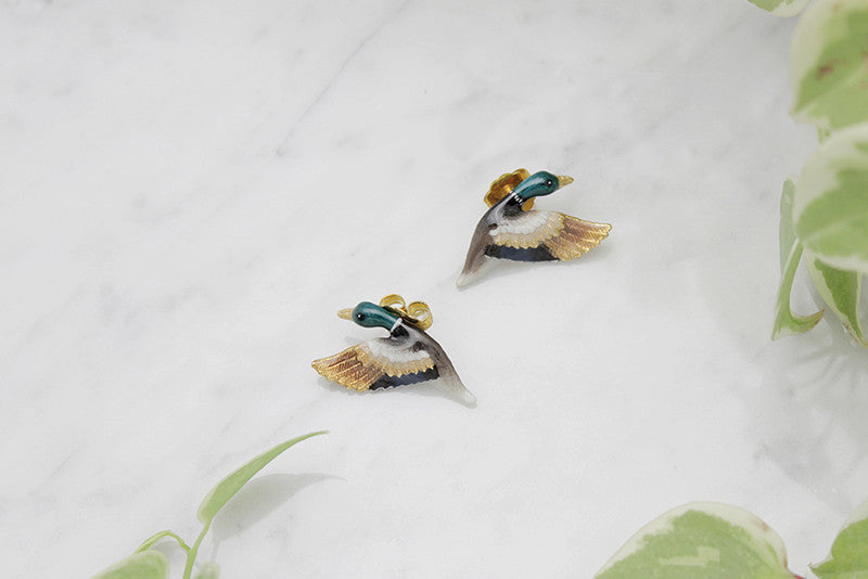 Beautiful mallard duck earrings, featuring colorful enamel detailing and gold accents, placed on a marble background.