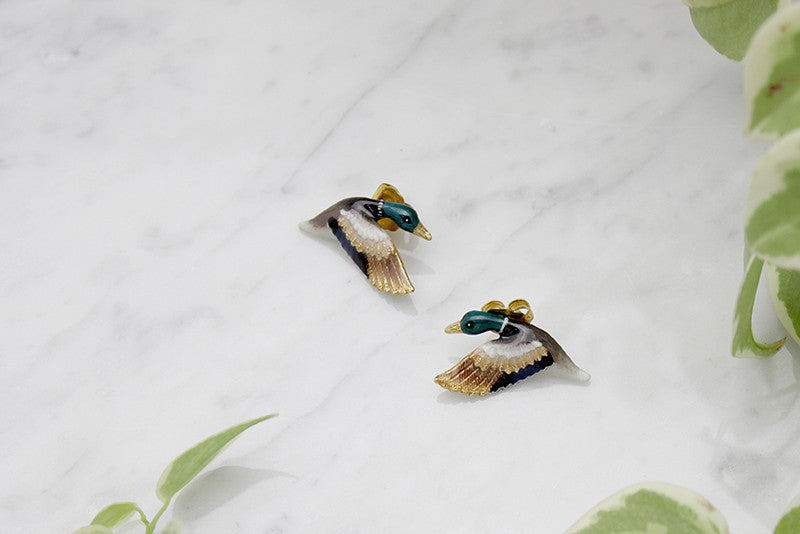 Beautiful mallard duck earrings, featuring colorful enamel detailing and gold accents, placed on a marble background.