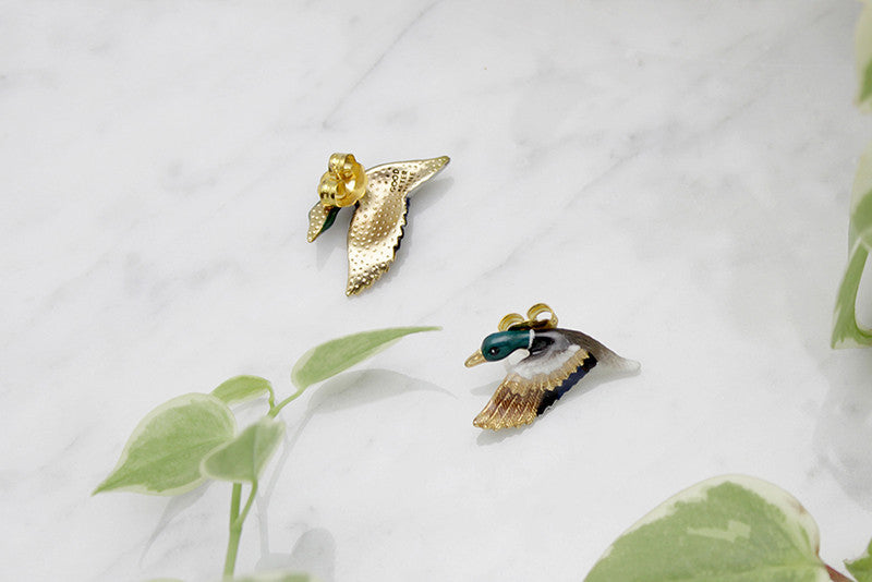 Beautiful mallard duck earrings, featuring colorful enamel detailing and gold accents, placed on a marble background.