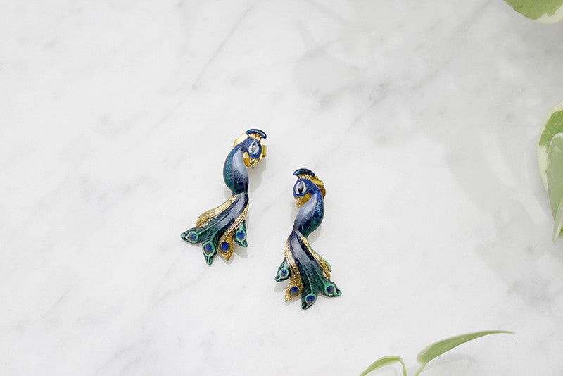 Unique peacock earrings with intricate feather details placed on a marble background.