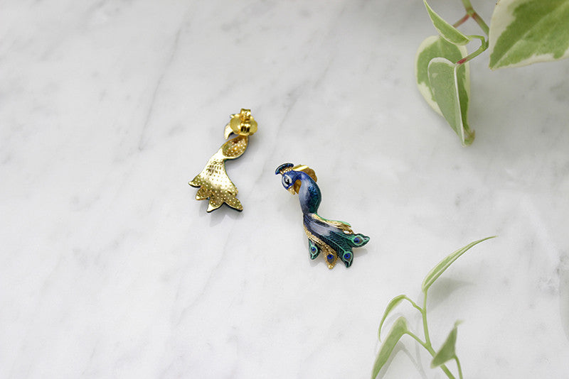 Stunning peacock earrings with intricate feather details placed on a marble background.