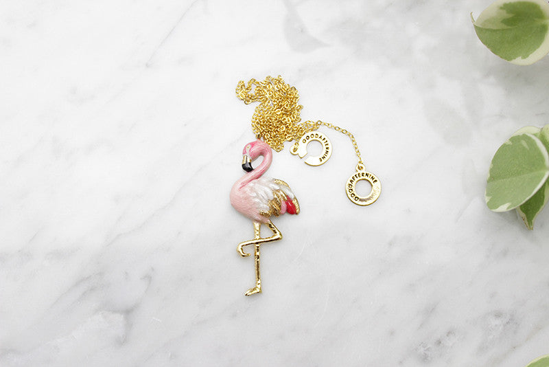 Stylish pink flamingo pendant on a gold chain placed on marble.