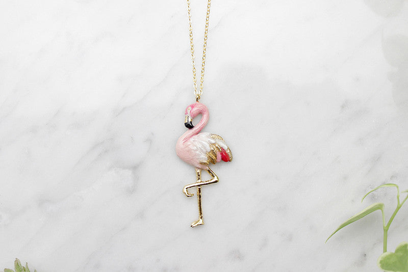 Stylish pink flamingo pendant on a gold chain placed on marble.