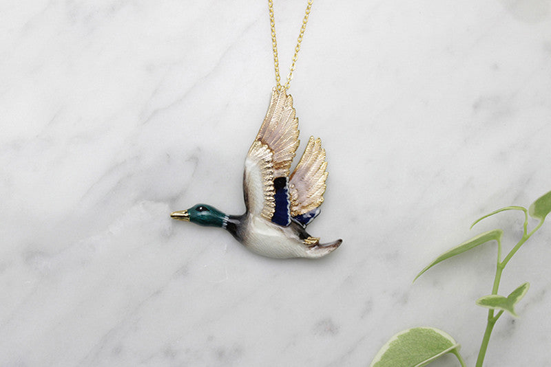 Beautifully crafted mallard duck pendant necklace with delicate detail, place on a marble background.