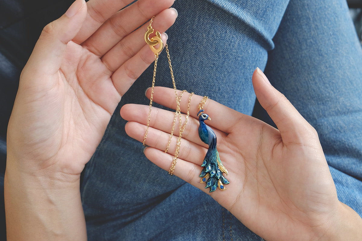 Close up of a hand showcasing a colourful peacock pendent necklace.