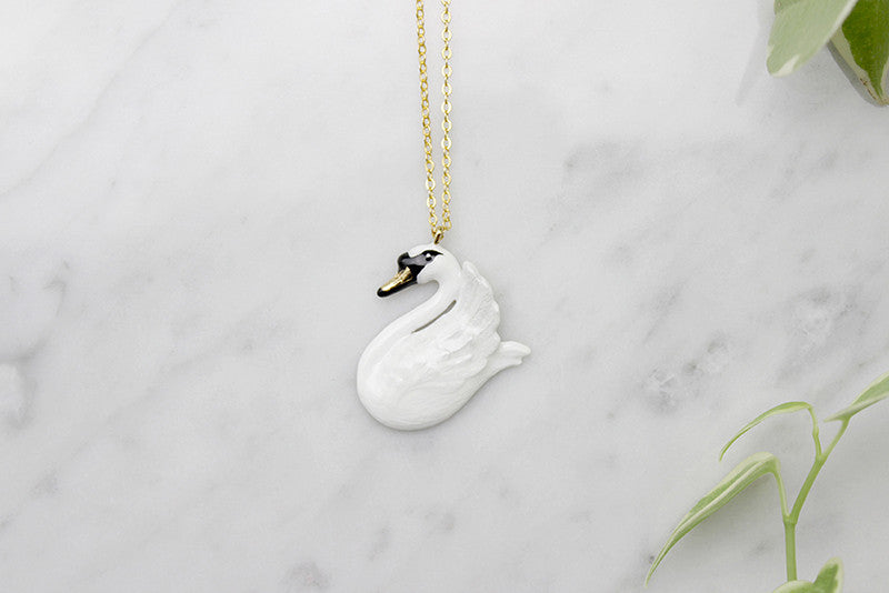 Beautiful swan pendant necklace placed on a marble background with green leaves.