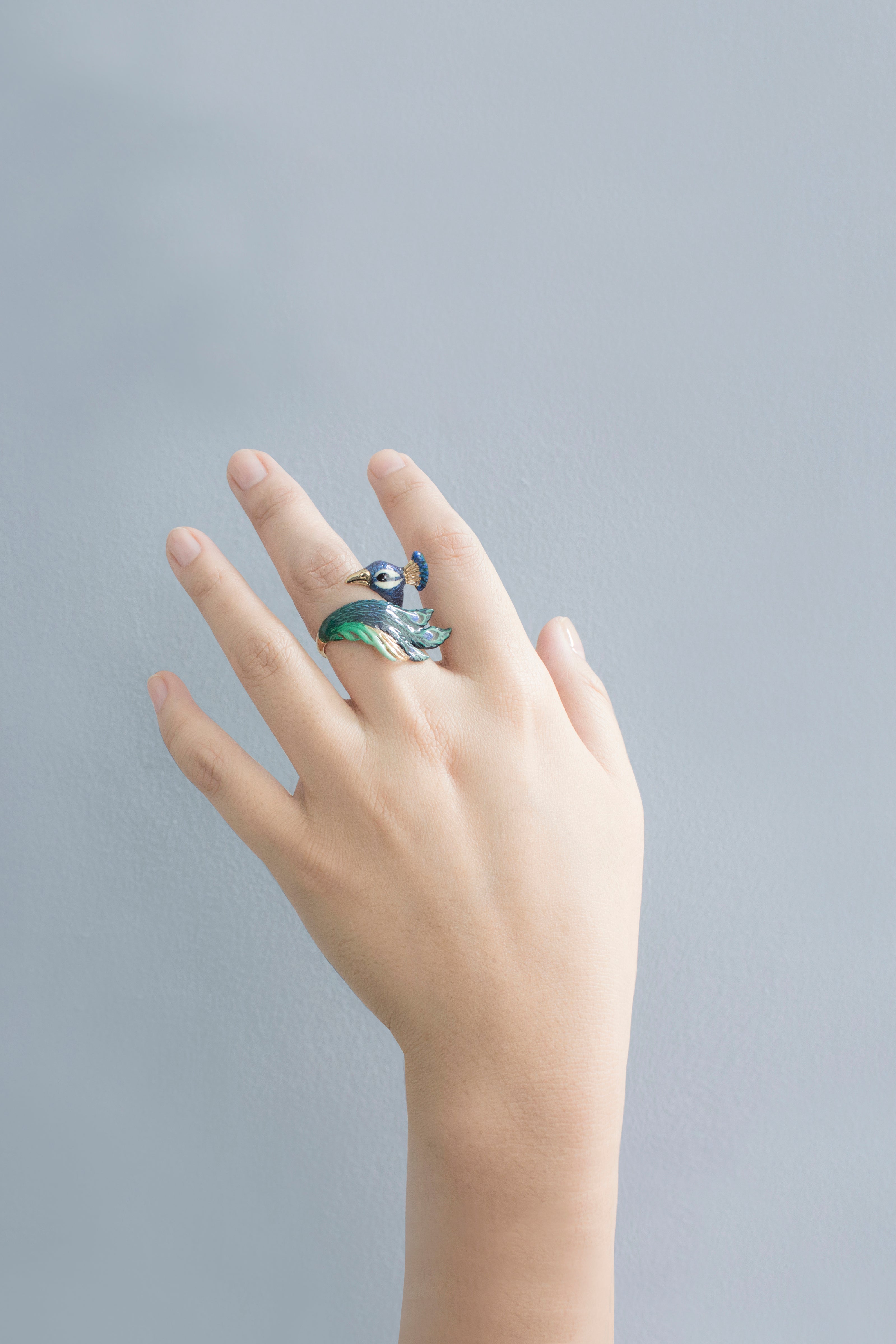 A hand wearing a stunning peacock ring with intricate details in blue and green.