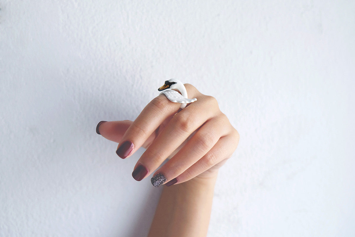 Close-up of hand with dark red nails polish showcasing a stunning white swan ring 