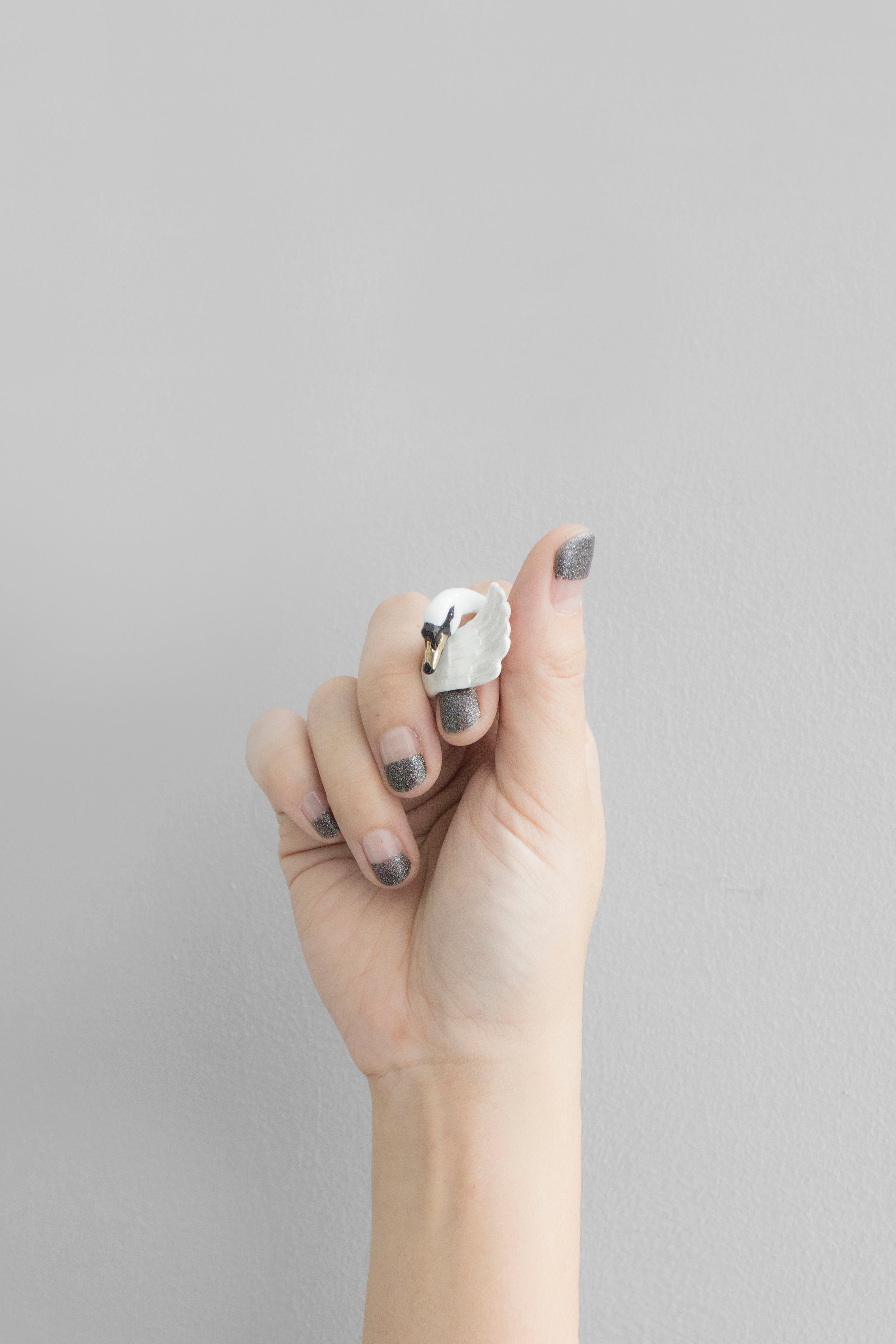 A hand with stylish nail polish showcasing a white swan ring