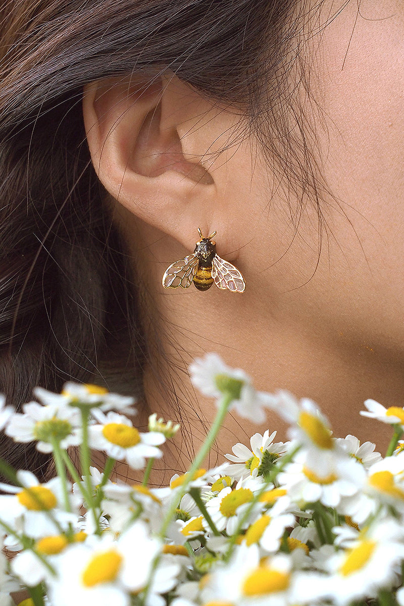 Close-up of charming bee earrings worn by a woman with flowers around.