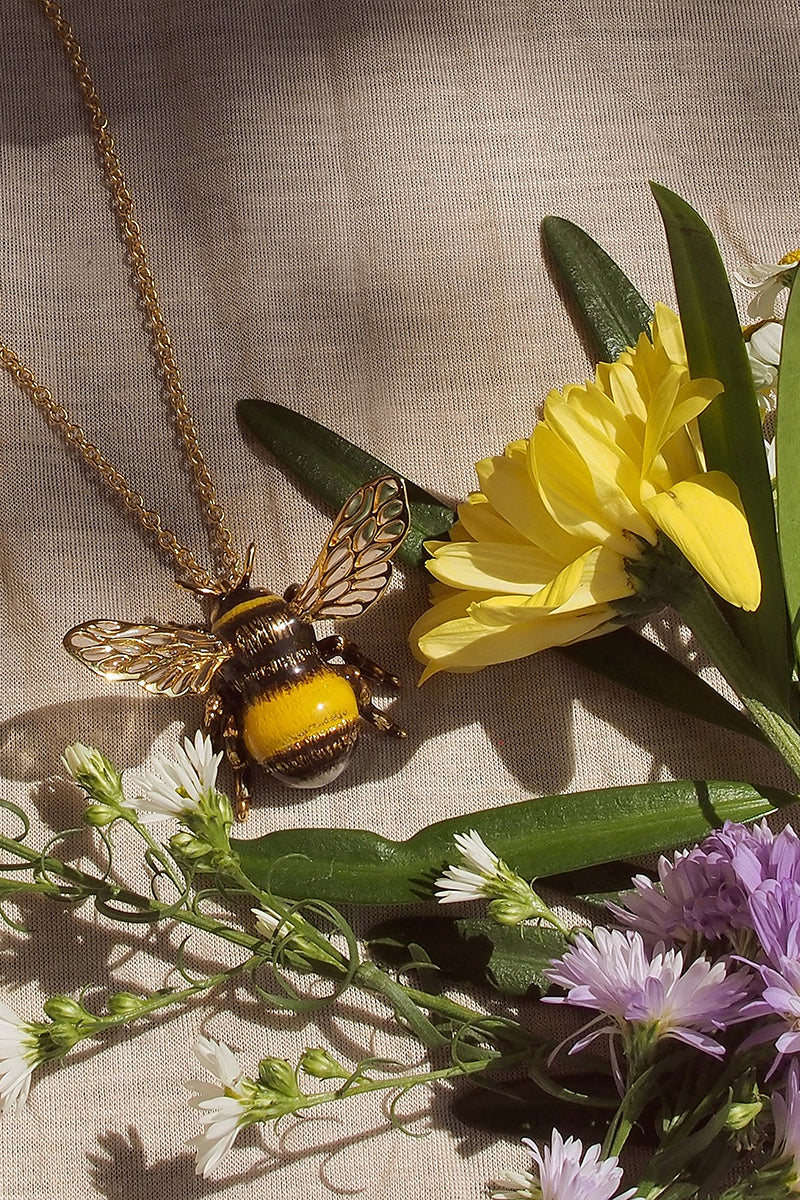 Handmade bee pendant necklace surrounded by flowers.