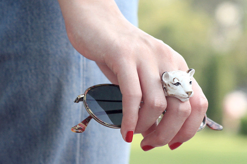 Close-up of a hand adorned with a adorable white bengal tiger ring holds a sun glasses.