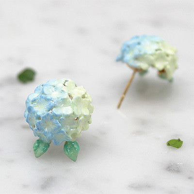 Artisan-crafted blue flower earrings with a delicate green leaf design placed on marble background.