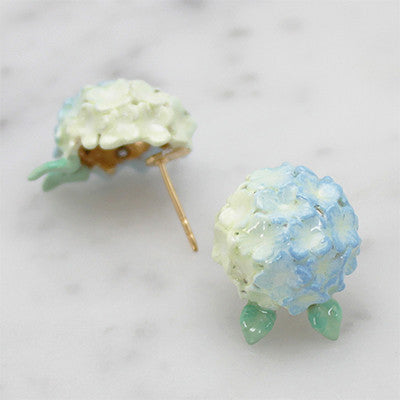 Artisan-crafted blue flower earrings with a delicate green leaf design placed on marble background.