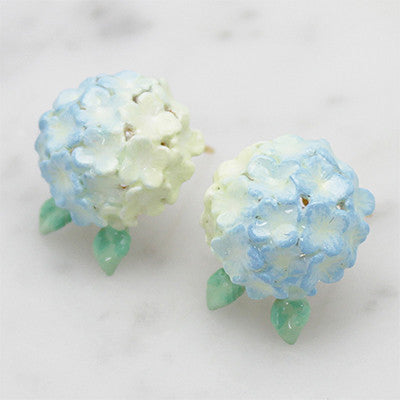 Artisan-crafted blue flower earrings with a delicate green leaf design placed on marble background.