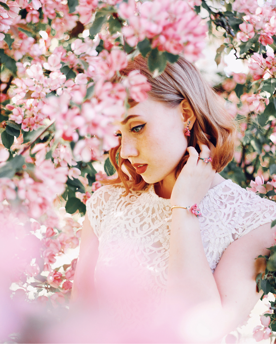 Close-up of a woman wearing floral jewelry amidst blooming flowers.