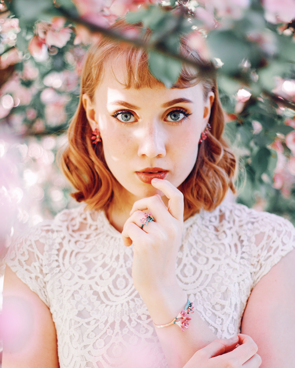 Portrait of a woman wearing delicate floral rings and bracelet.