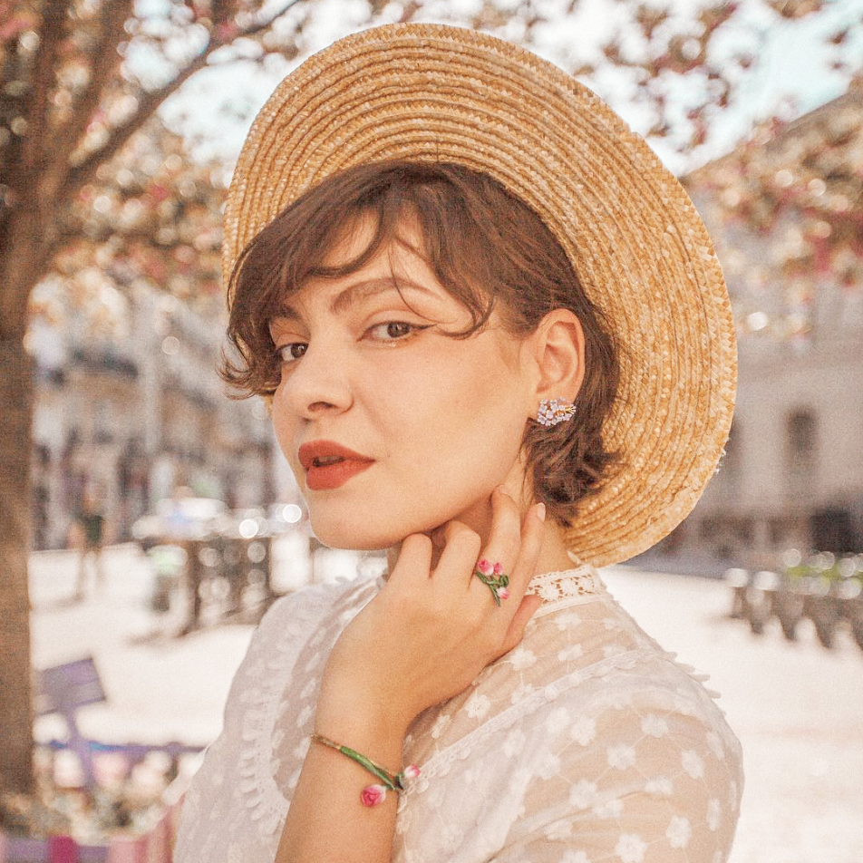 A woman in a straw hat wearing floral earrings, a floral bracelet, and a floral ring,  ideal for summer look.