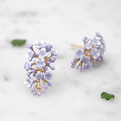 Purple floral earrings with delicate petals placed on a marble background.