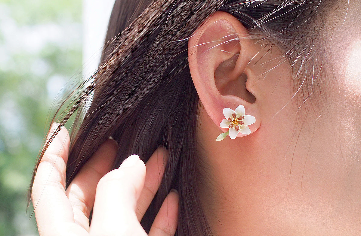 A close-up of a woman's ear adorned with a white lily earring, ideal for summer fashion.