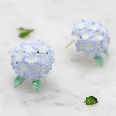 Artisan-crafted flower earrings with a delicate green leaf design placed on marble background.