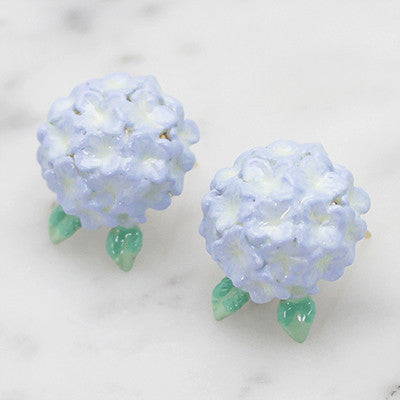 Artisan-crafted flower earrings with a delicate green leaf design placed on marble background.