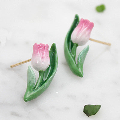 Charming floral earrings featuring pink tulip and green leaves, placed on a marble background.