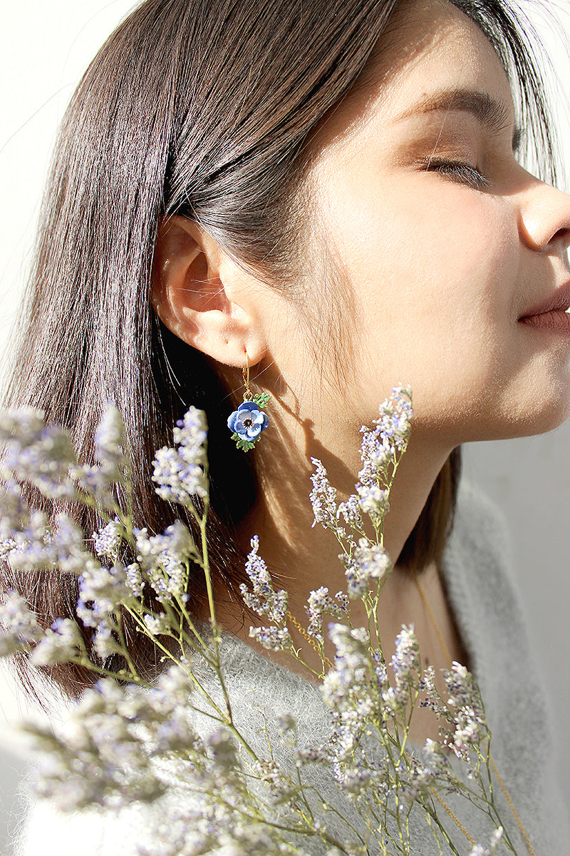 Close-up of a model wearing purple flower earrings with flowers in the foreground.