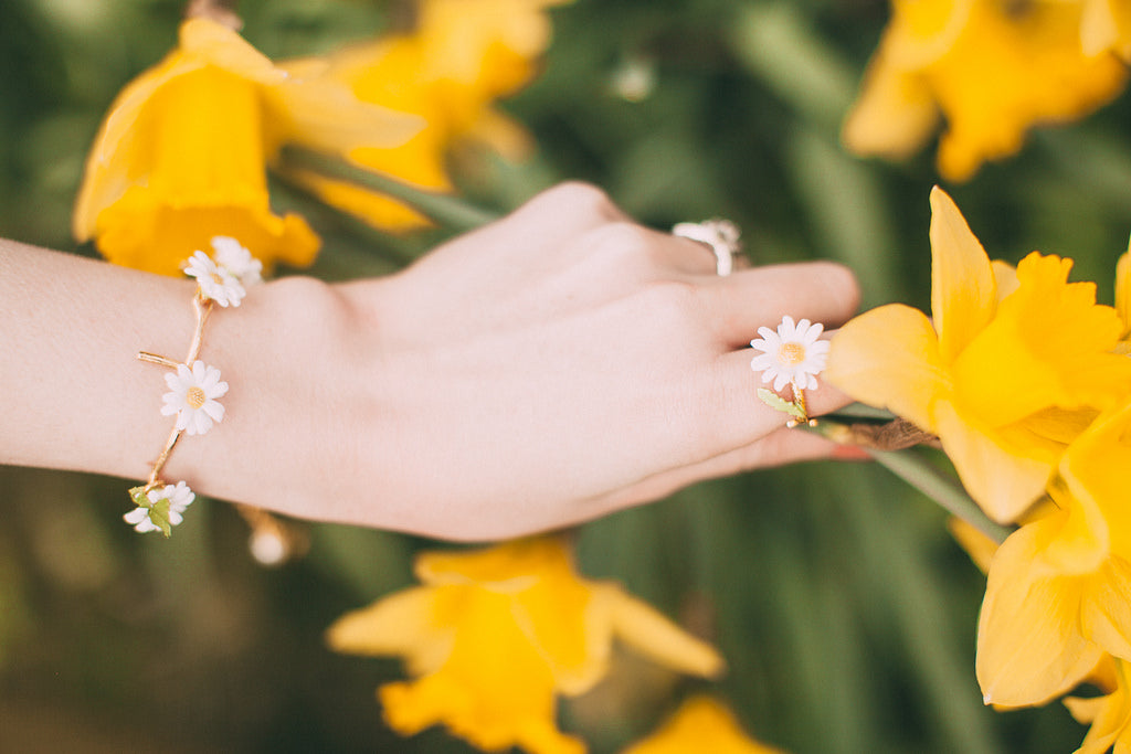 Close-up of a hand wearing a daisy bracelet and ring surrounded by yellow flowers