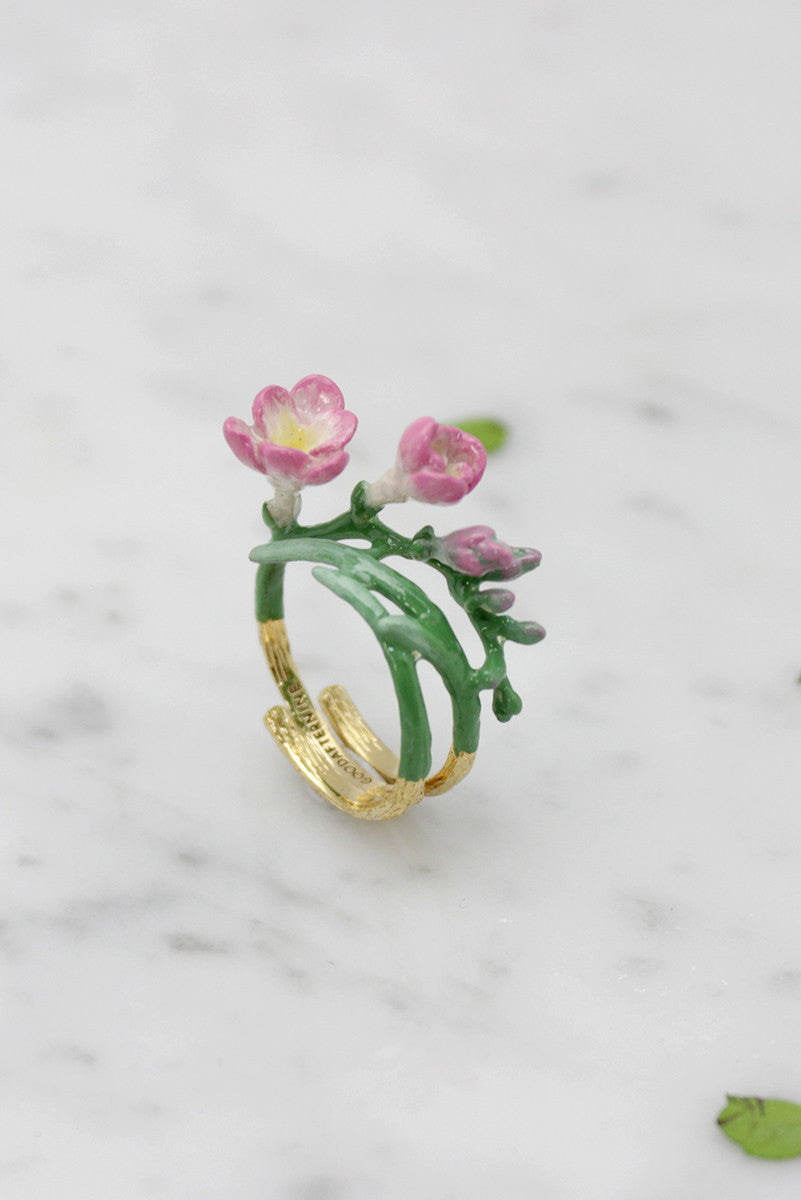 A unique botanical-inspired ring with pink blossoms and a gold band, placed on marble background.