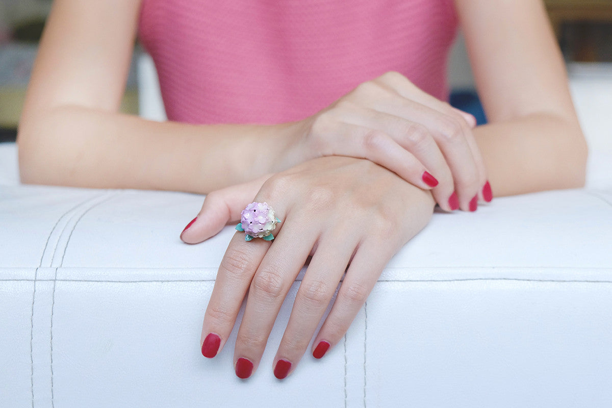 Close-up of a hydrangea flower ring on a hand with red nails.