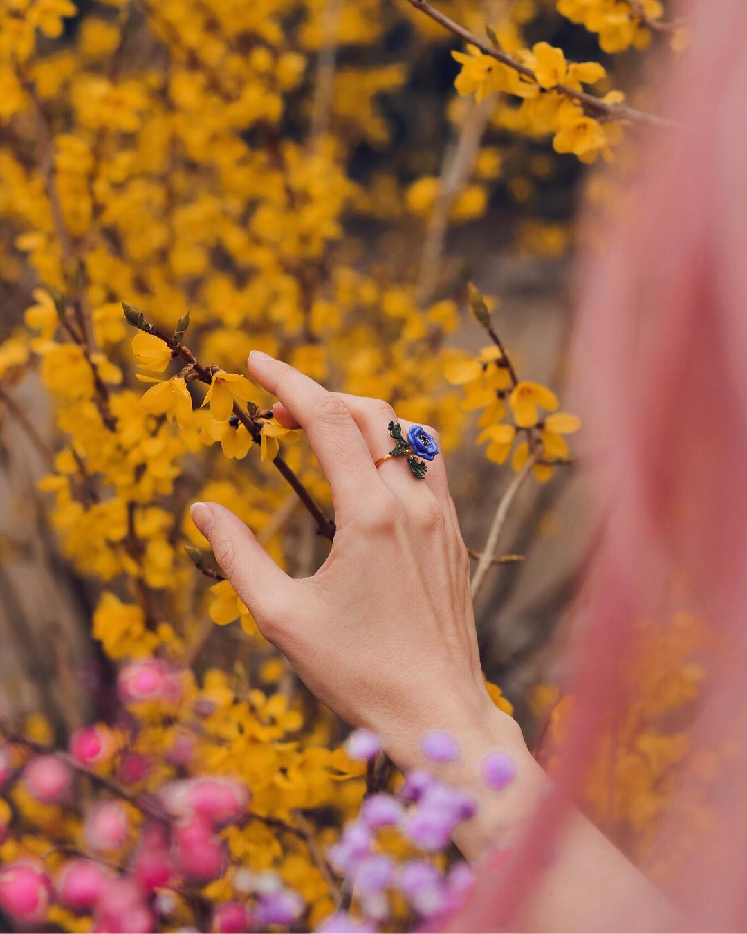 A hand with a purple flower ring amidst blooming colorful flowers.