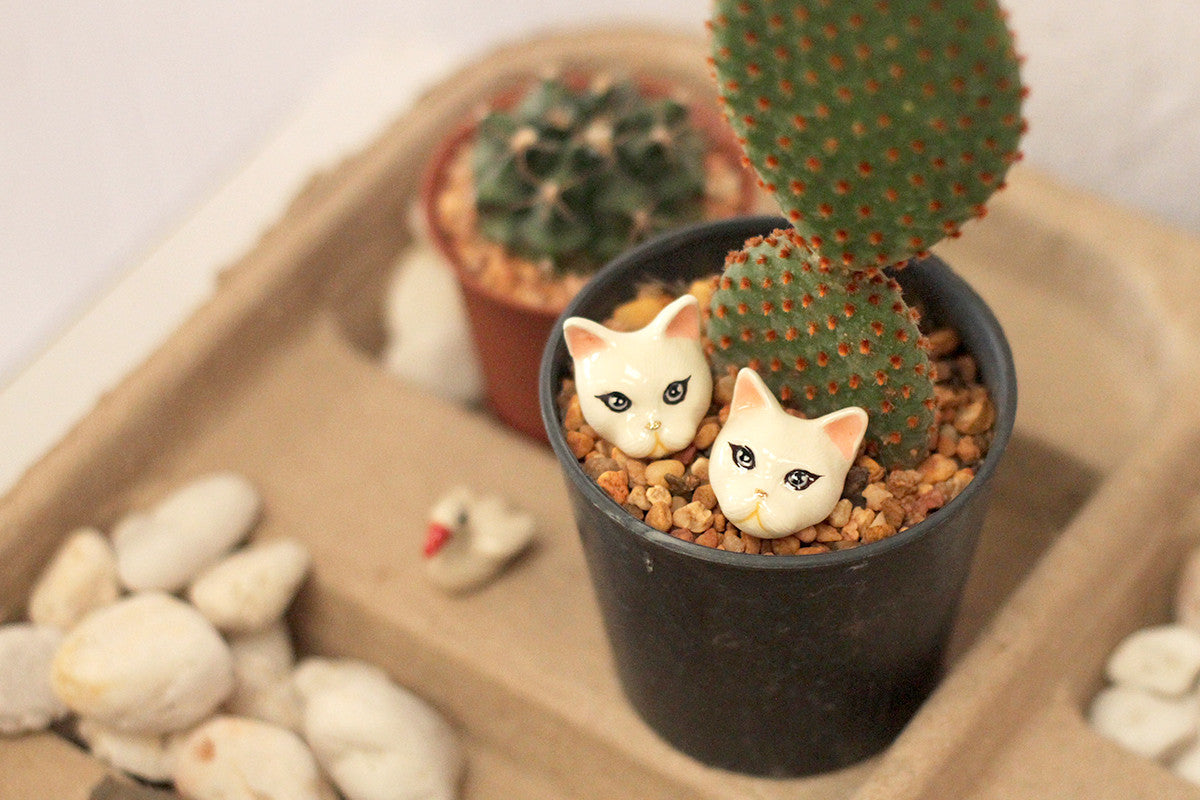 Adorable white Persian cat earrings placed in a pot of cactus.