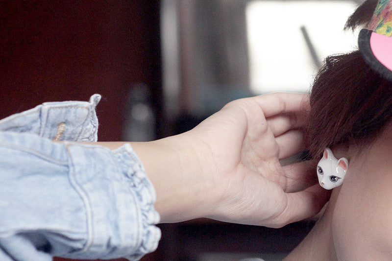 A hand gently places a whimsical cat-shaped earring on a person’s earใ