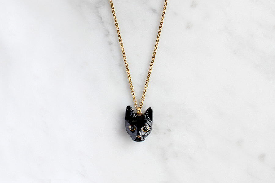 Charming gold necklace with black cat's head pendant, placed on a marble background.