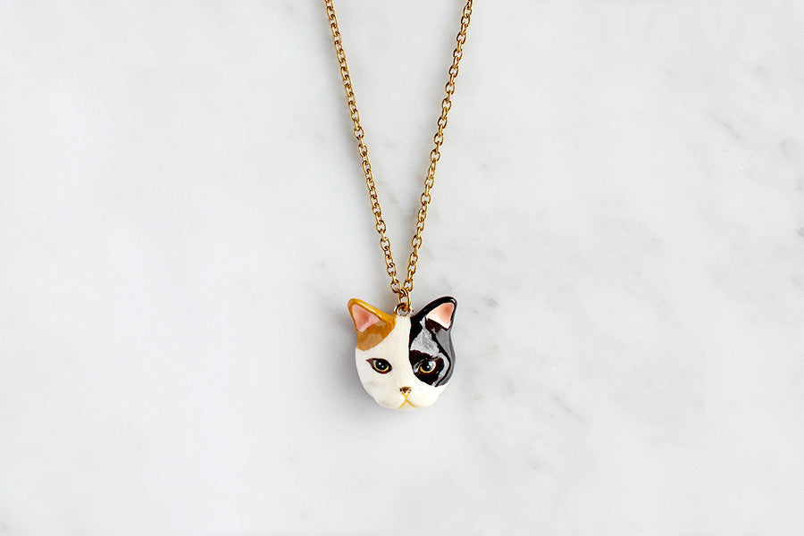 Unique cat head pendant necklace with artistic design placed on marble background.