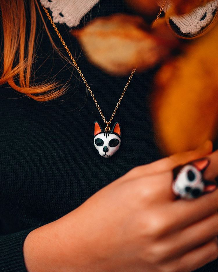 Cat skull necklace and ring worn by a person with long hair, held among autumn leaves.