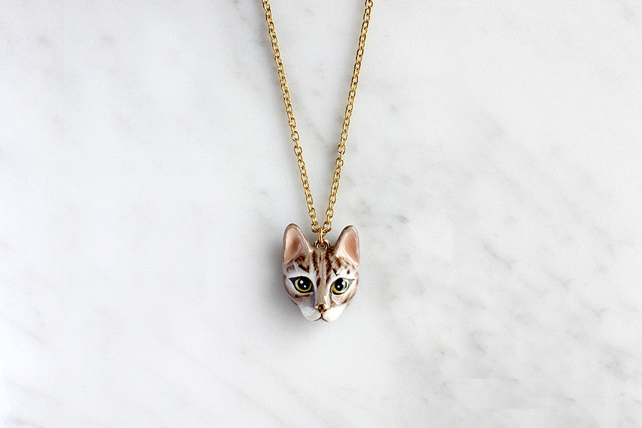 Adorable tabby cat pendant necklace placed on marble background.