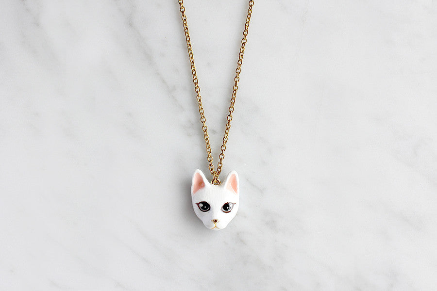 Adorable gold necklace with white cat's head pendant, perfect for cat lovers.