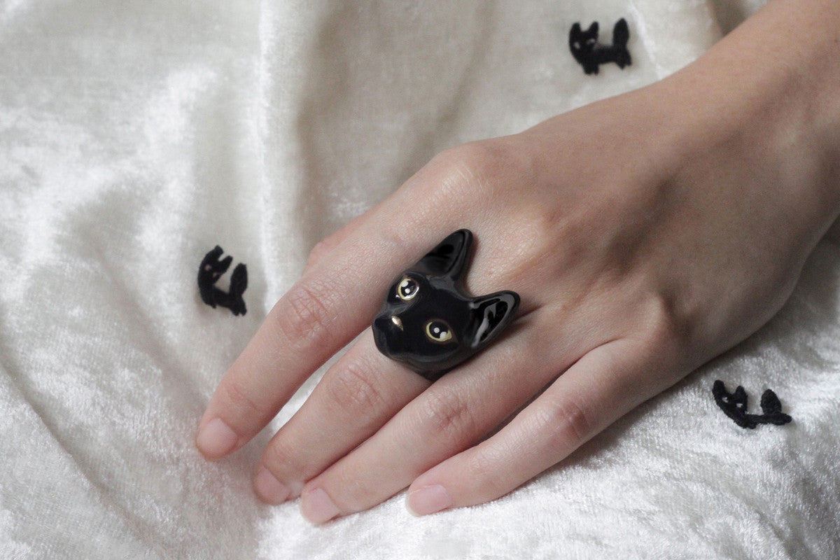 A close-up of a hand wearing a cute black cat ring test on a white fabric.