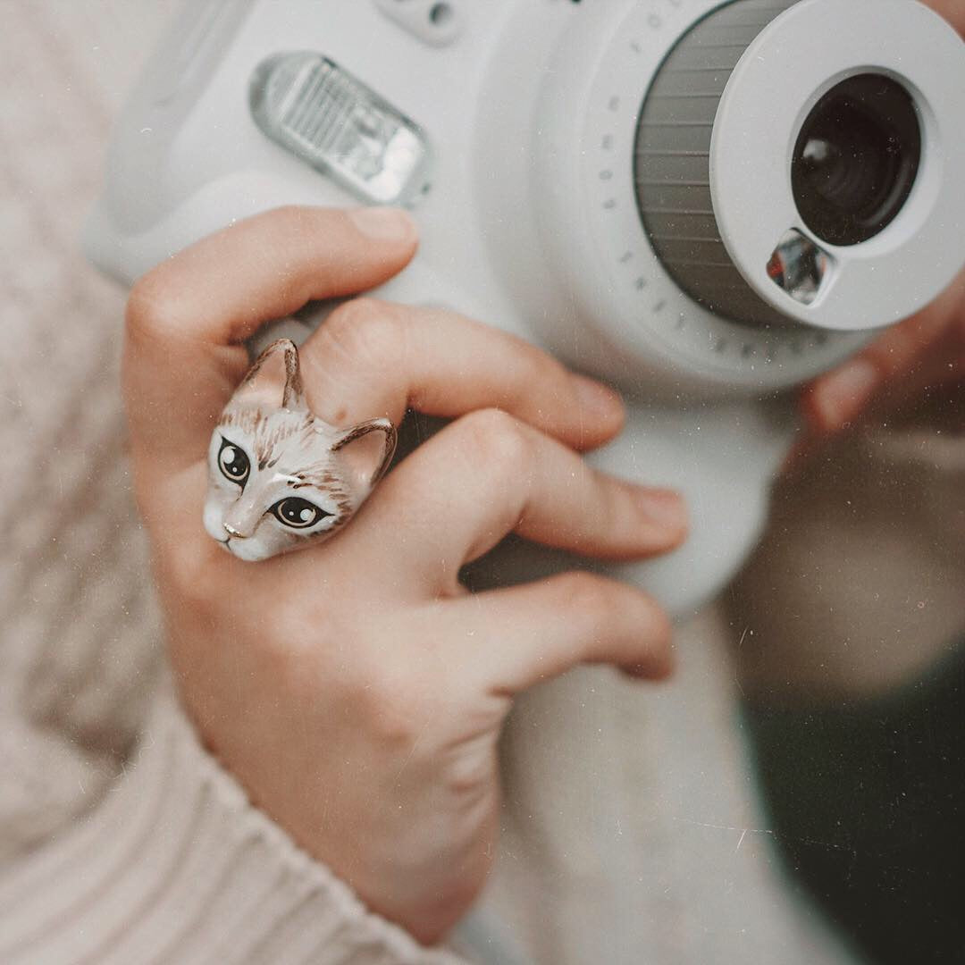 A close-up of a hand wearing a adorable cat ring while holding a camera.