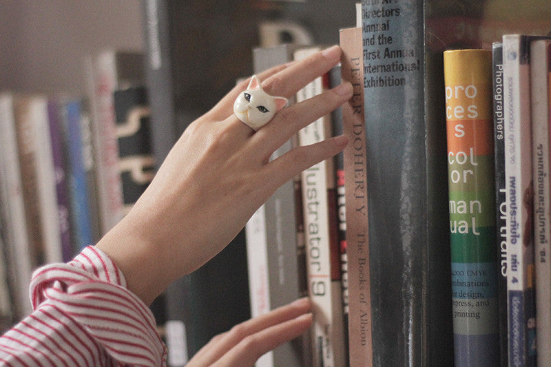 Hand with an adorable cat-shaped ring reaching for books on a shelf.