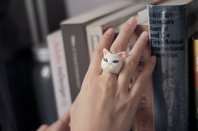 A close-up of a hand with an adorable cat-shaped ring reaching for books on a shelf.