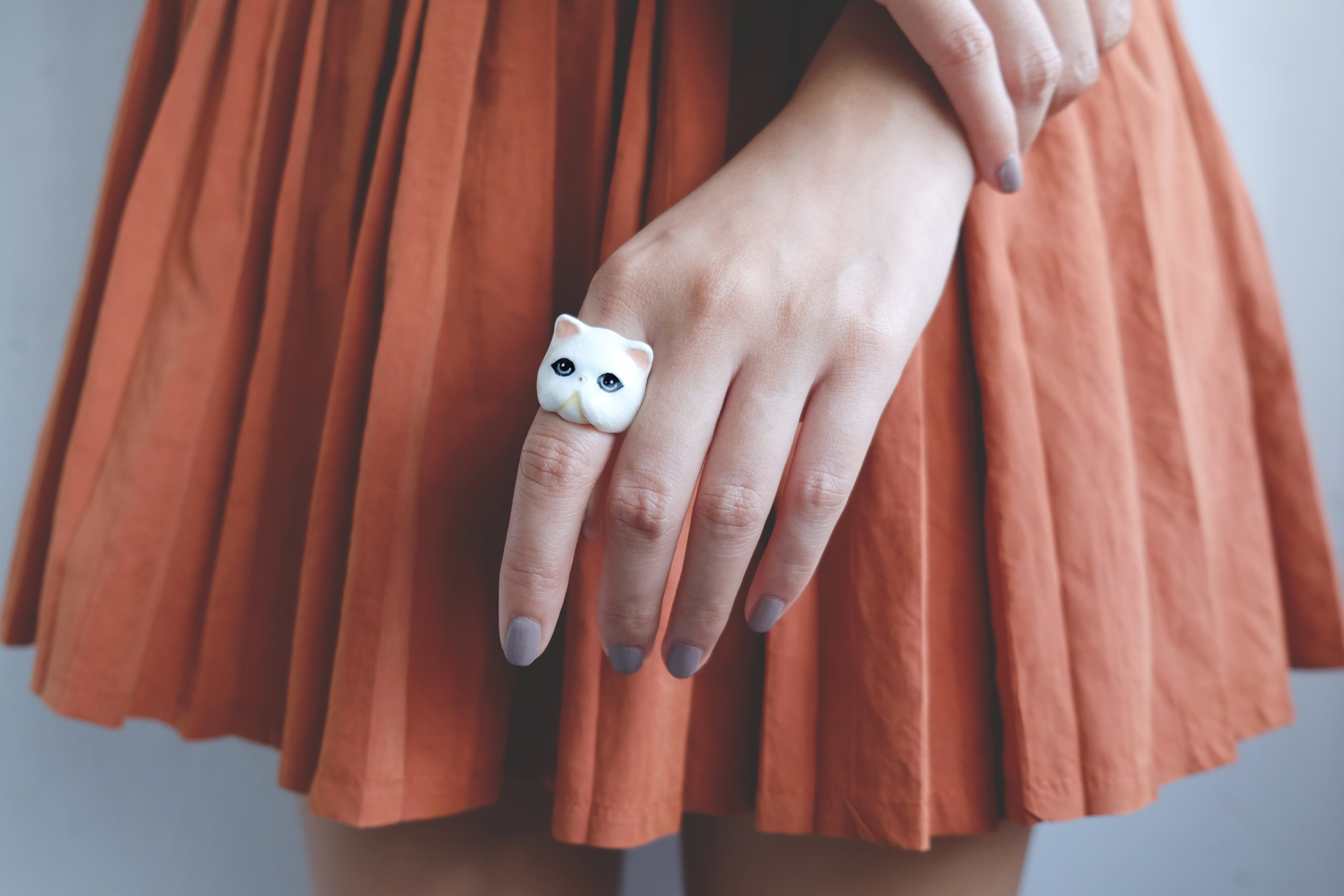 Unique white cat ring on a finger, accentuating a playful and stylish outfit with an orange skirt.